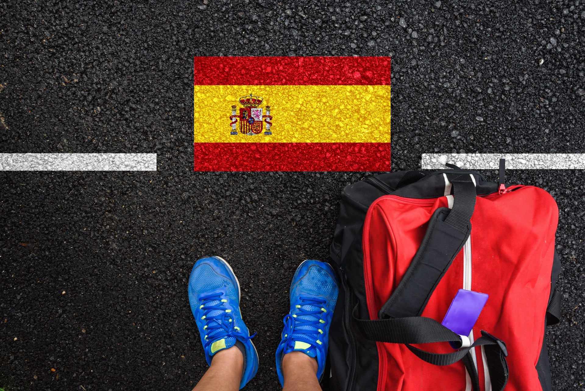 a man with a shoes and travel bag is standing on asphalt next to flag of Spain and border